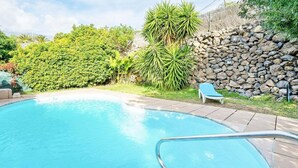 A swimming pool with a stone wall and greenery. - Romantic Getaway in Malpais de Candelaria (Malpais de Candelaria)
