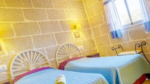 A room with two beds, a stone wall, a window with curtains, and a wall-mounted light fixture. - Romantic Getaway in Malpais de Candelaria (Malpais de Candelaria)