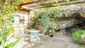 A patio with a stone wall, a table with chairs, and potted plants. - Romantic Getaway in Malpais de Candelaria (Malpais de Candelaria)