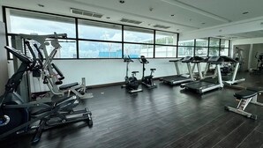Ett gym med olika typer av träningsutrustning, stora fönster och utsikt över byggkranar.