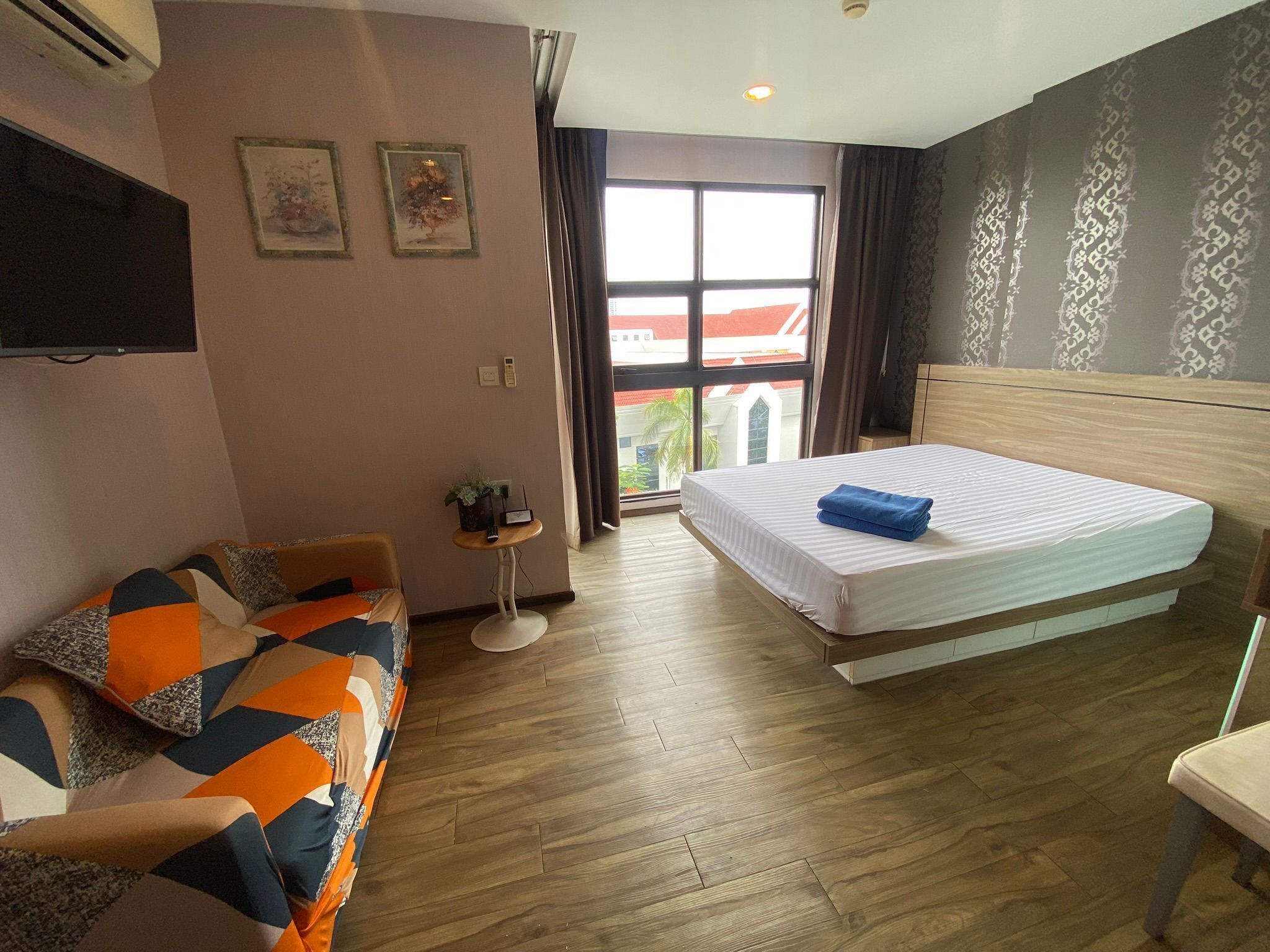 A hotel room with a bed, a sofa, a small table with a plant, and a TV mounted on the wall.