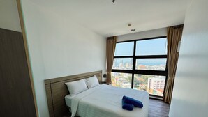 Ett hotellrum med en stor säng, en sänggavel i trä, utsikt över staden genom ett stort fönster och ett trägolv.