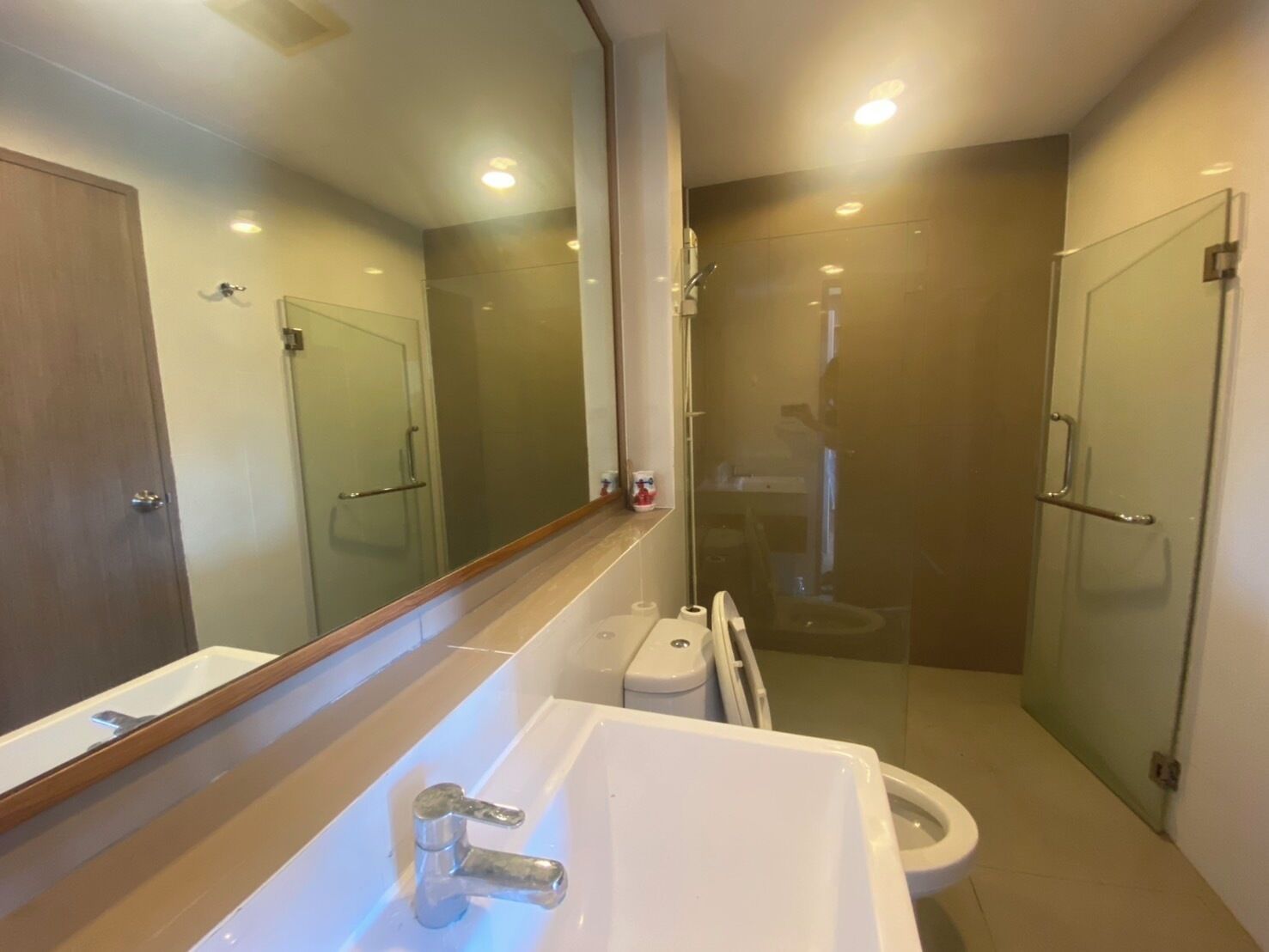 A modern bathroom with a large mirror, a sink, a toilet, and a glass-enclosed shower area.
