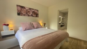 A bedroom with a large bed, a nightstand with a lamp, a painting on the wall, and a bathroom visible through an open door. - A nature lover's paradise: walks and relaxation at the gîte (Chamelet)
