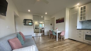 A modern living room with a grey sofa, a dining area with a white table and colorful chairs, and a kitchen with white cabinets and a stove. - A nature lover's paradise: walks and relaxation at the gîte (Chamelet)