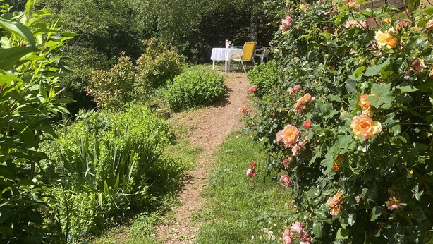 A garden path leading to a table and chairs, surrounded by lush greenery and flowering plants. - A nature lover's paradise: walks and relaxation at the gîte (Chamelet)