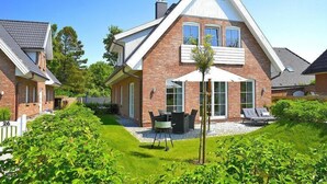 A modern two-story house with a brick exterior, a sloped roof, and a patio with outdoor furniture. - Ferienwohnung in Wyk auf Foehr (Wyk auf Föhr)
