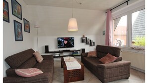 Un salon avec deux canapés marron, une table basse en bois, un téléviseur et des tableaux encadrés accrochés au mur.