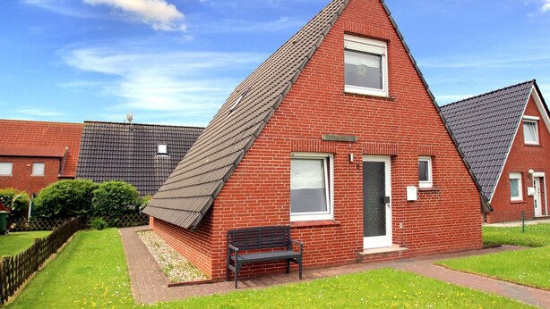 Une maison en briques rouges, avec un toit en pente, une porte d’entrée et un banc dans la cour.