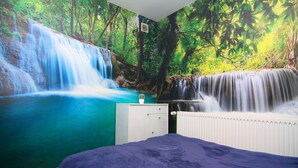 A bedroom with a large mural of a waterfall and forest, a white dresser, and a blue bedspread. - Ferienwohnung am Prüßsee in Güster (Güster)