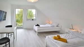 Une chambre moderne, décorée dans des tons de blanc, comprenant un bureau, deux lits et de grandes fenêtres donnant sur un paysage verdoyant.