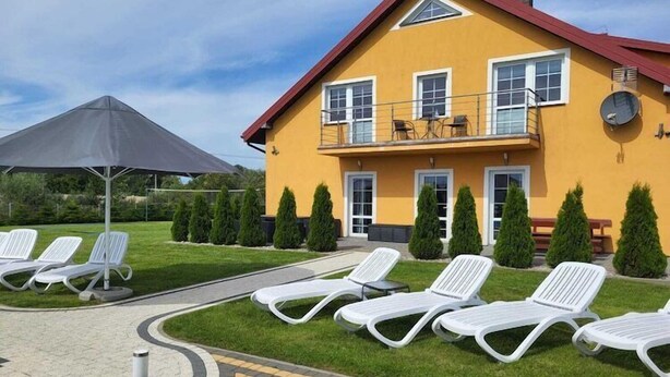 Un edificio giallo con tetto rosso, un balcone con mobili da esterno e poltrone da relax bianche su una zona pavimentata.