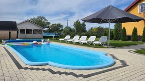 Una piscina esterna con bordo piastrellato, circondata da lettini e una zona coperta.
