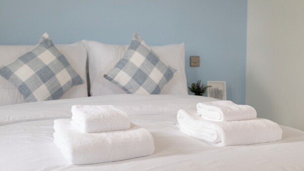 A neatly made bed with white linens and folded towels, blue and white checkered pillows, and a light blue wall. - Charming Frome Retreat With 4 Bedrooms (Frome)
