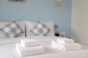 A neatly made bed with white linens and folded towels, blue and white checkered pillows, and a light blue wall. - Charming Frome Retreat With 4 Bedrooms (Frome)