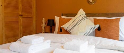 A neatly made bed with white linens and towels, a wooden wardrobe, and a wall-mounted mirror.