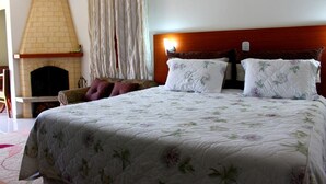 A bedroom with a large bed, a wooden headboard, a fireplace, and a window with curtains. - POUSADA BELA VISTA (Camanducaia)