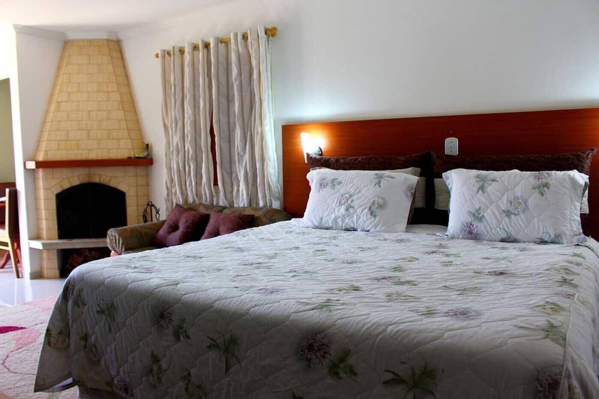 Ein Schlafzimmer mit einem großen Bett, einem hölzernen Kopfteil, einem Kamin und einem Fenster mit Vorhängen.