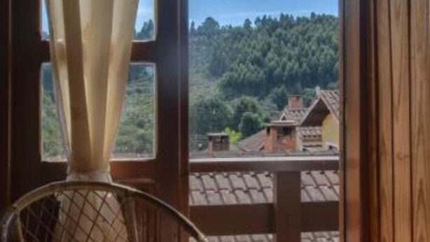 A wooden balcony with a view of a forested hill and houses. - POUSADA BELA VISTA (Camanducaia)