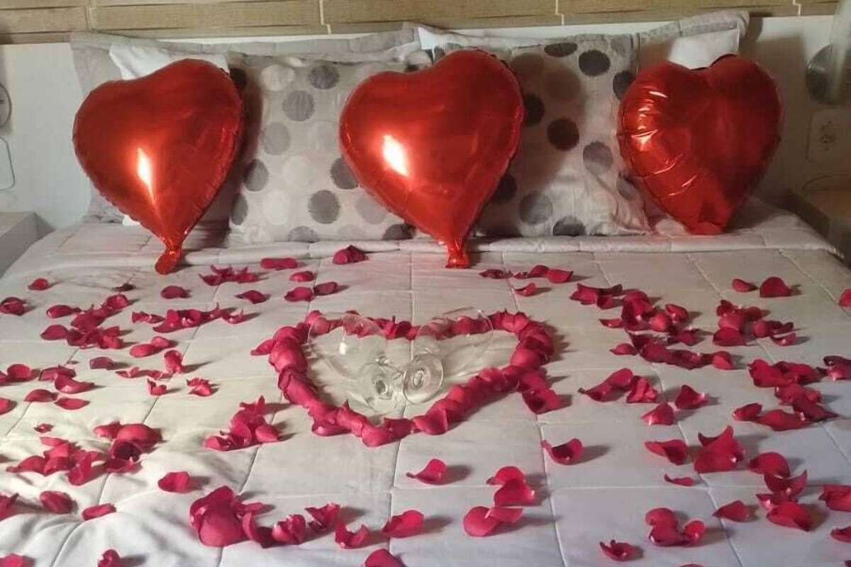 Ein Bett mit einer herzförmigen Anordnung aus Rosenblättern und drei roten, herzförmigen Luftballons.