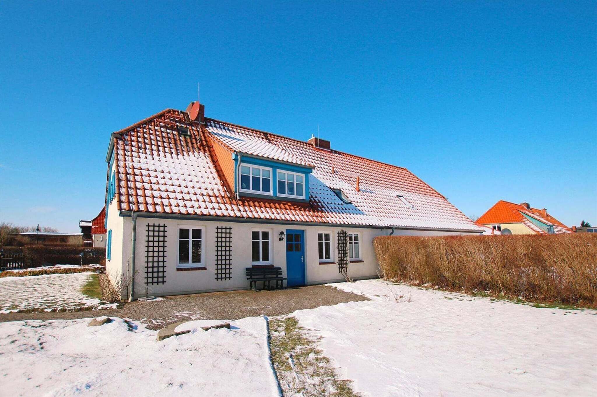Uma casa térrea com telhado de telhas vermelhas, uma porta azul e um pequeno alpendre com um banco.