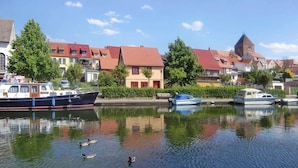 A calm river with boats and ducks, surrounded by traditional houses with red roofs and a church tower.