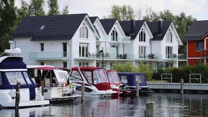 A row of modern houses with balconies, a dock with boats, and a calm water body.