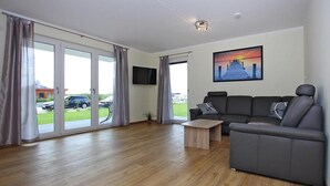 A modern living room with a grey sofa, a wooden coffee table, and a TV mounted on the wall.