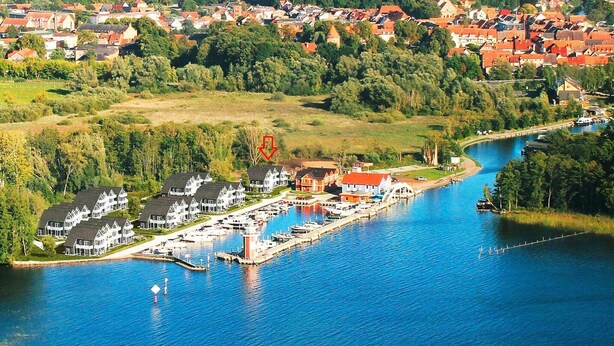 A marina with docked boats, a lighthouse, and residential buildings along a river.