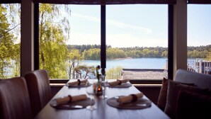 Une table à manger dressée pour quatre personnes, avec vue sur un lac et une forêt, grâce à de grandes fenêtres.