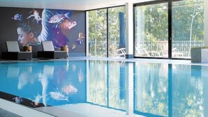 Une piscine intérieure ornée d’une fresque murale, dotée de grandes fenêtres et offrant une vue sur l’extérieur.