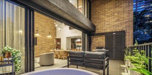 A modern outdoor living area with a hot tub, seating, and a kitchen visible through glass doors. - Modern apt High Ceilings, BBQ - Morph 401 (Medellín)