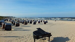 Une plage bordée de rangées de chaises de plage rayées, avec un grand piano posé sur le sable.