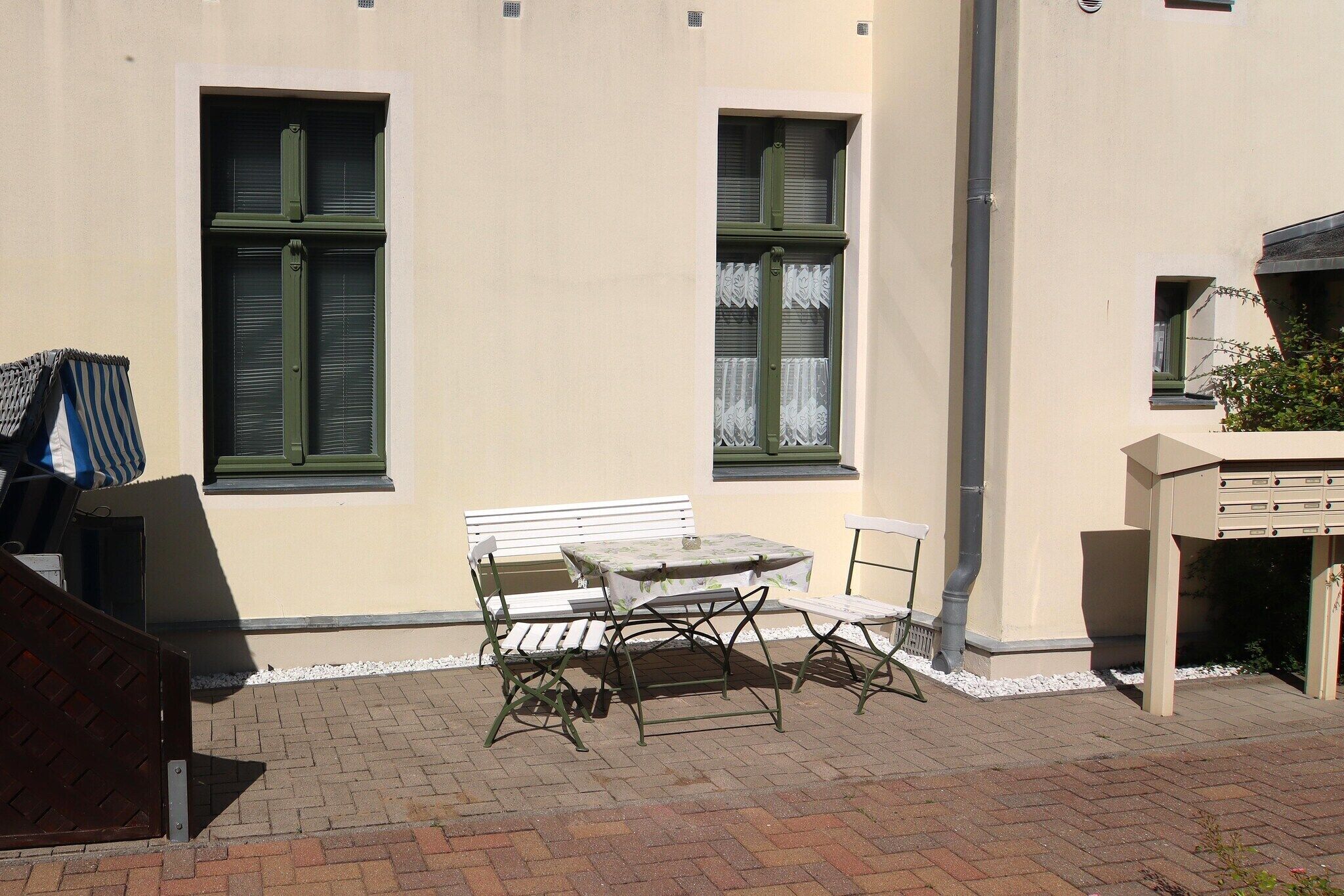 An outdoor patio with a table and chairs, a white bench, and a small garden area.