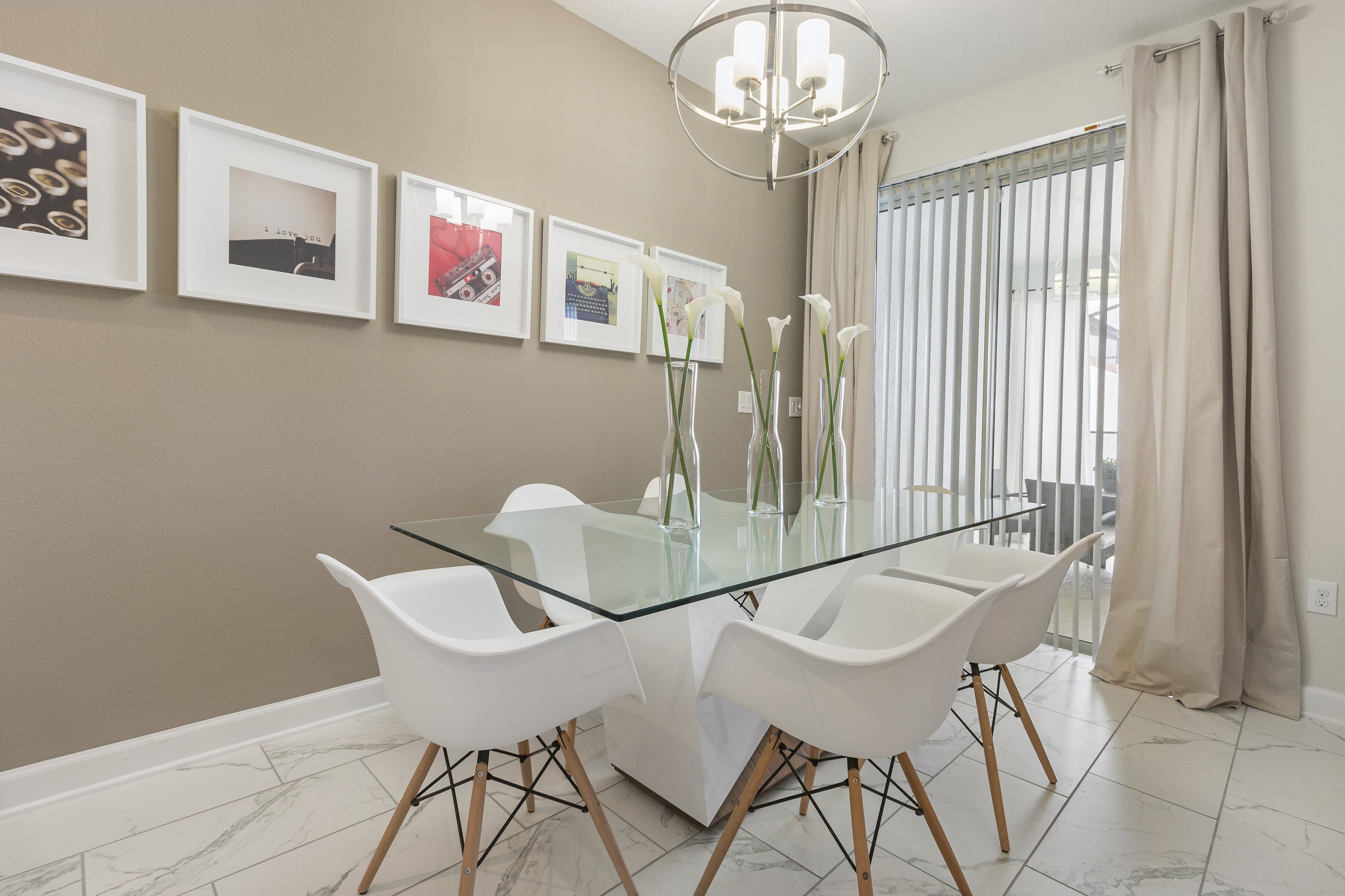A dining area with a glass table, white chairs, and framed pictures on the wall.