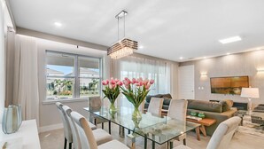 A modern living room with a glass dining table, comfortable seating, a large window, and a flat-screen TV. - Last Minute Disney! Private Pool, Hot Tub, Game Room & Themed Bedrooms. Book Now! #65867 (Orlando)