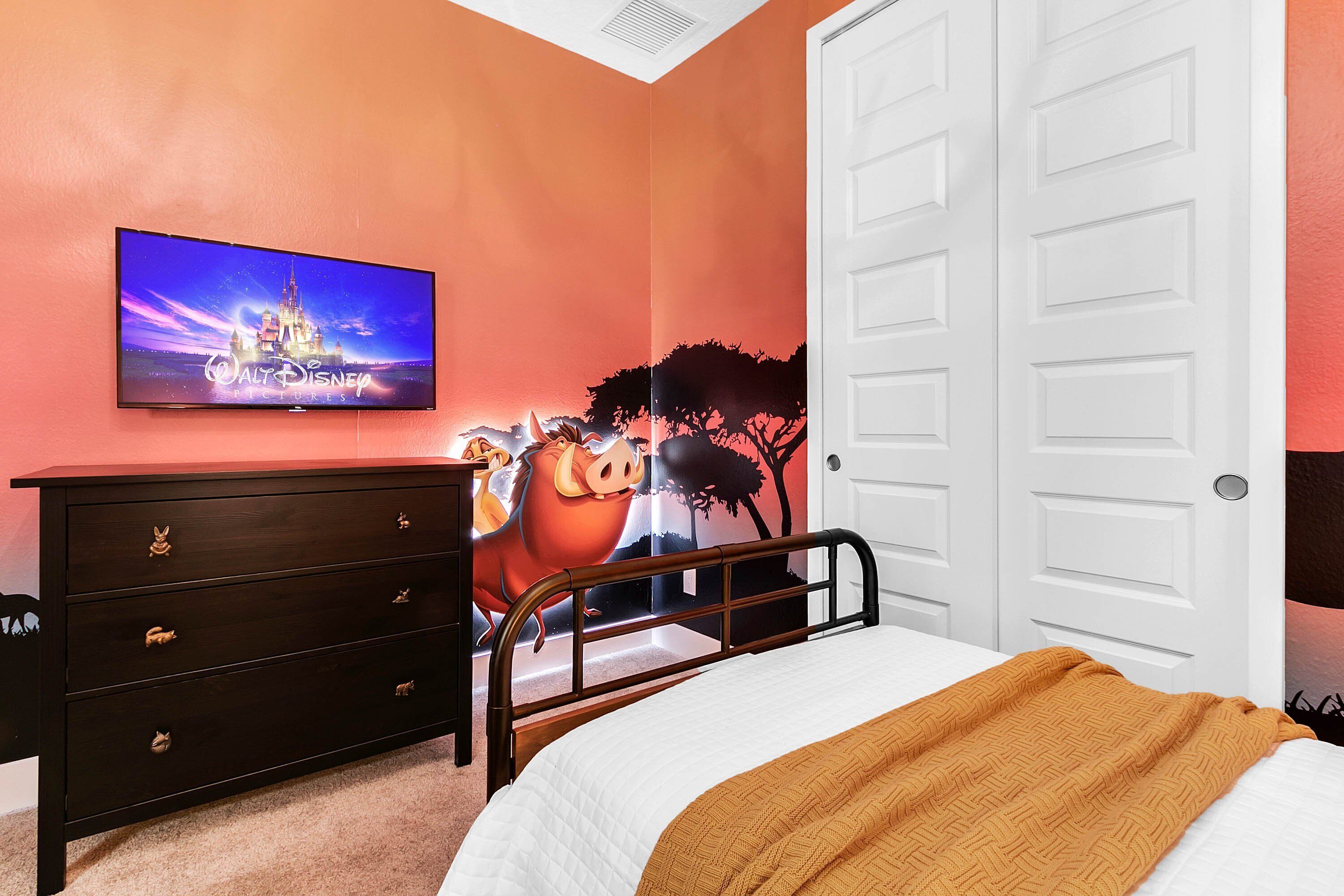 A bedroom with a bed, a dresser, a television on the wall, and a door.