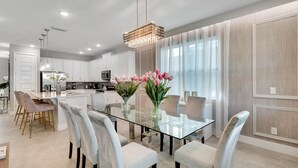 A modern kitchen with white cabinets, a glass dining table, and a chandelier. - Last Minute Disney! Private Pool, Hot Tub, Game Room & Themed Bedrooms. Book Now! #65867 (Orlando)