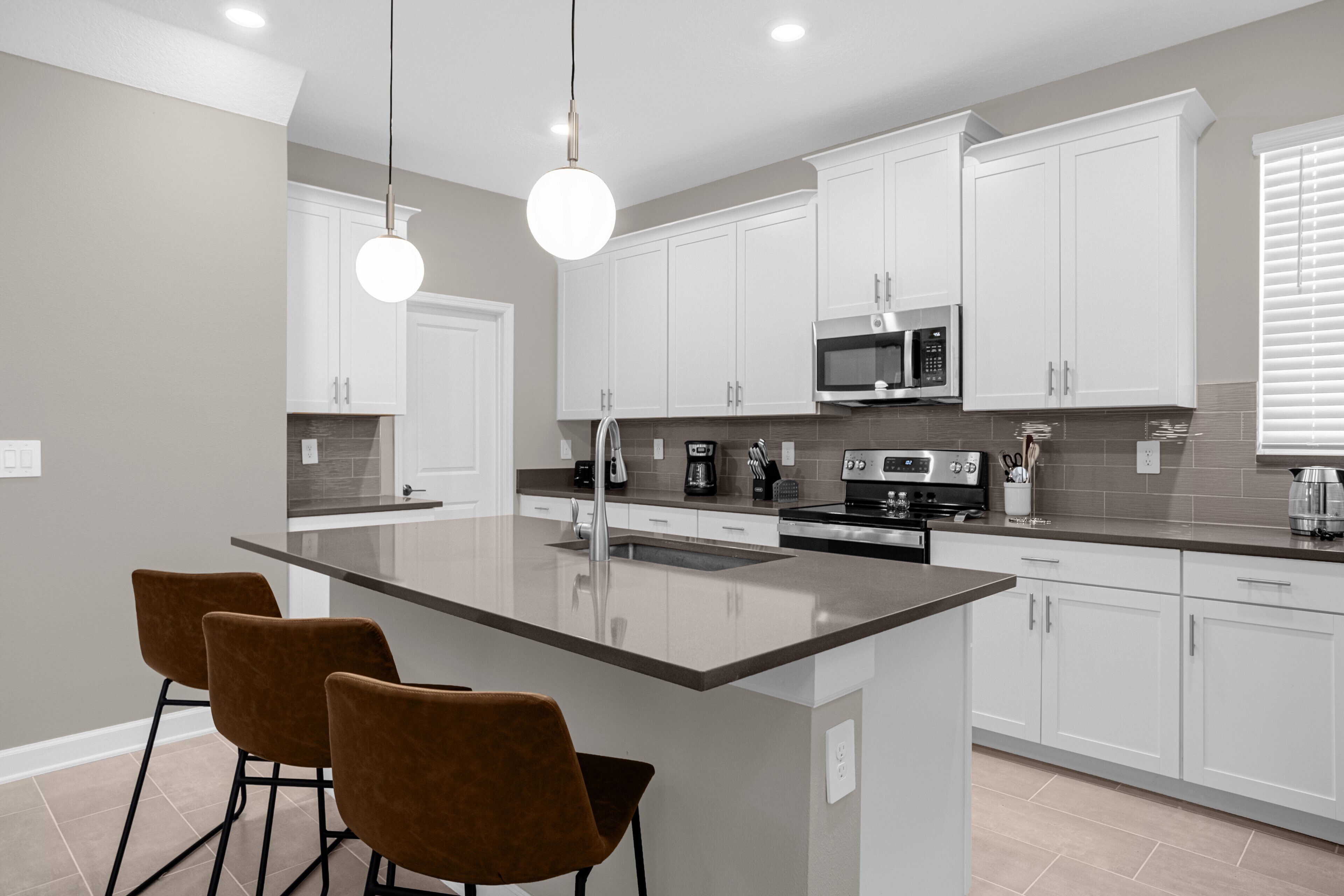 A modern kitchen with white cabinets, a central island with bar stools, stainless steel appliances, and pendant lighting.