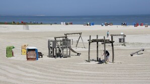 Una playa con una zona arenosa, estructuras de juego de madera y cabañas de playa numeradas.