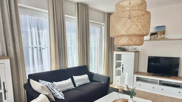 Una sala moderna con un sofá oscuro, una mesa de centro blanca y un televisor sobre un mueble de madera.