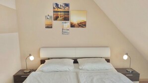 Un dormitorio con una cama, dos mesitas de noche y tres cuadros colgados en la pared.