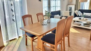 Un comedor con una mesa y sillas de madera, un lámpara colgante y vistas al exterior a través de un ventanal.