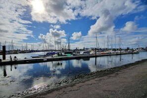 A marina with multiple boats docked, calm water, and a clear sky.