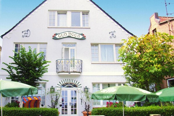 A white building with a sign reading "GUD KOOB" and a balcony with a wrought iron railing.
