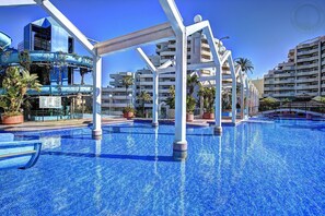 A swimming pool with clear blue water, surrounded by white pillars and potted plants. - Front Sea View Apartment Large Terrace (Benalmádena)
