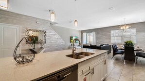 A modern kitchen with a built-in dishwasher, a large island with a sink, and a dining area with a table and chairs. - Last Minute Disney Getaway! Townhouse with Private Pool. Book Now! #65787 (Orlando)