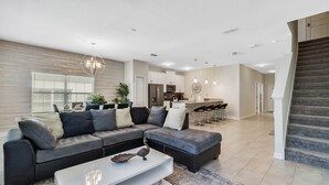 A modern living room with a sectional sofa, a coffee table, and a kitchen in the background. - Last Minute Disney Getaway! Townhouse with Private Pool. Book Now! #65787 (Orlando)