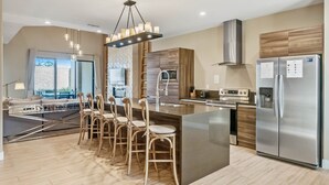 A modern kitchen with a central island, stainless steel appliances, and a dining area with wooden chairs. - Last Minute Disney Getaway! Luxury Villa with Private Pool. Book Now! #66003 (Orlando)