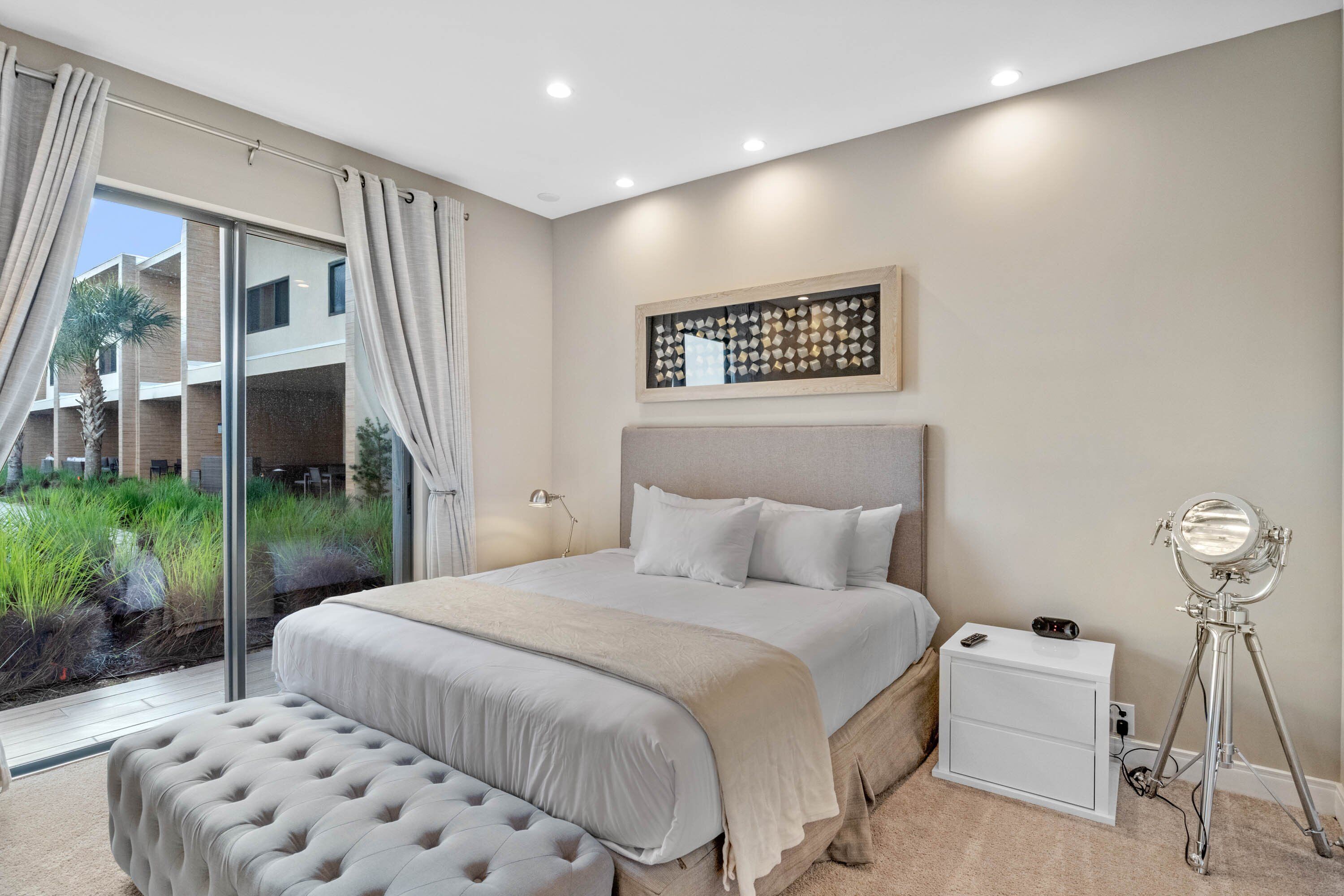 Een slaapkamer met een groot bed, een nachtkastje, een lamp en een spiegel op een statief.